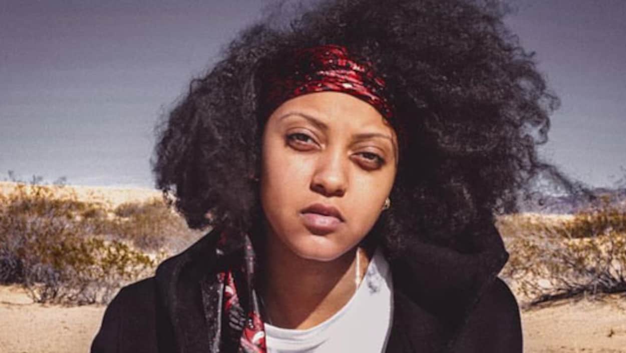 Naya Ali avec un bandeau rouge dans les cheveux, devant un paysage désertique.