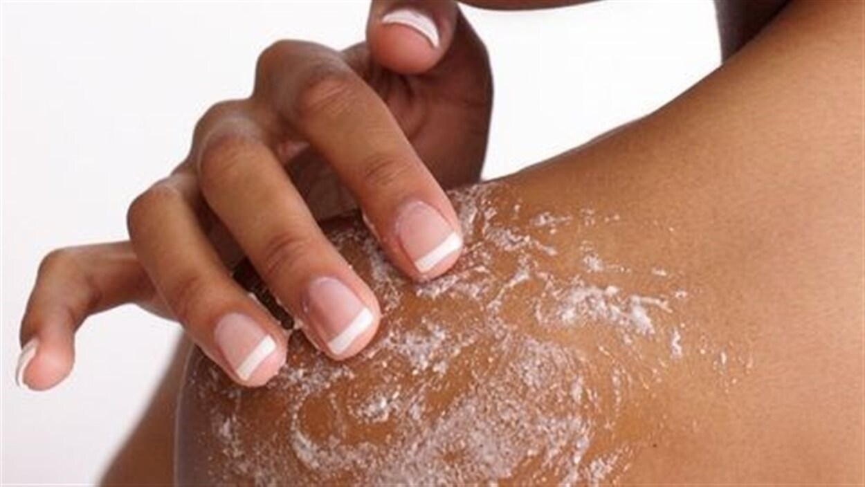 L'épaule d'une femme en gros plan, elle y applique une crème hydratante.