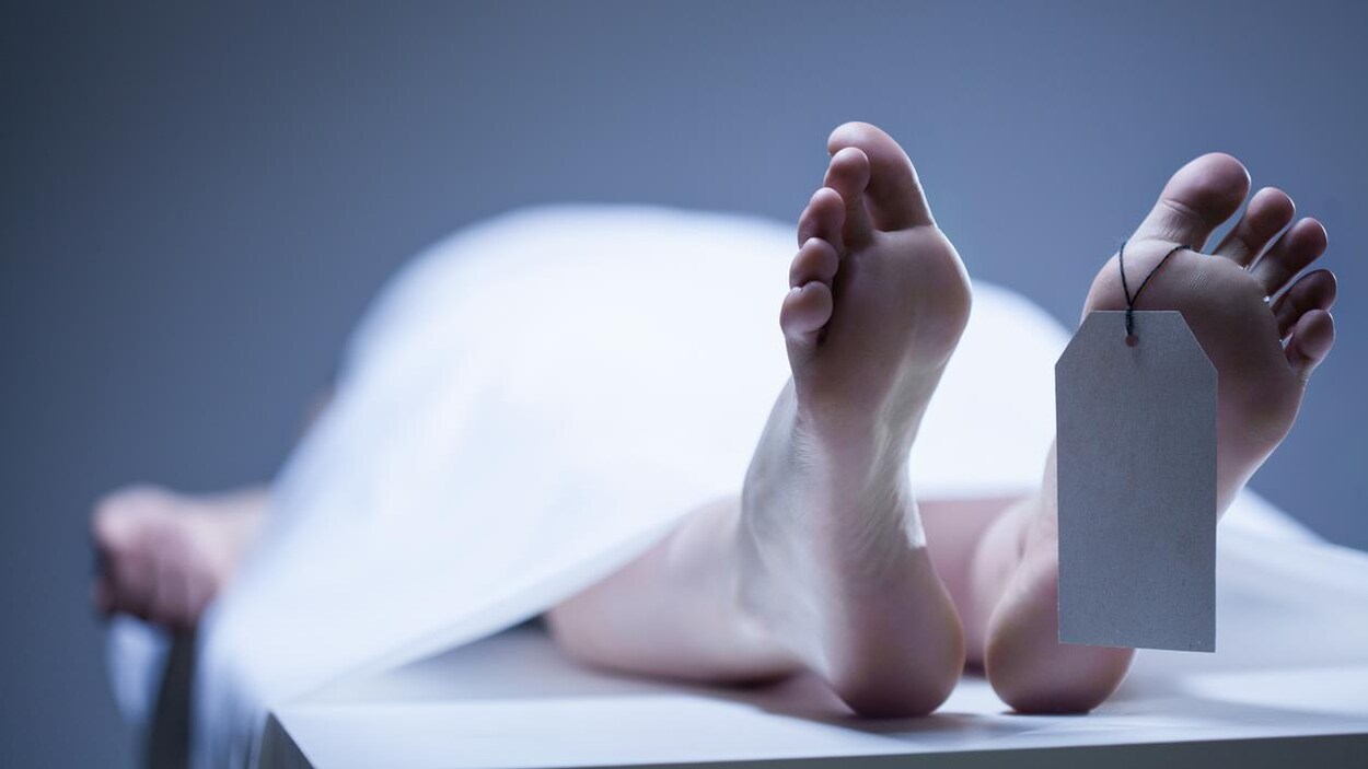 Photo des pieds d'une personne allongée sur une table recouverte d'un drap, avec une étiquette au pied.