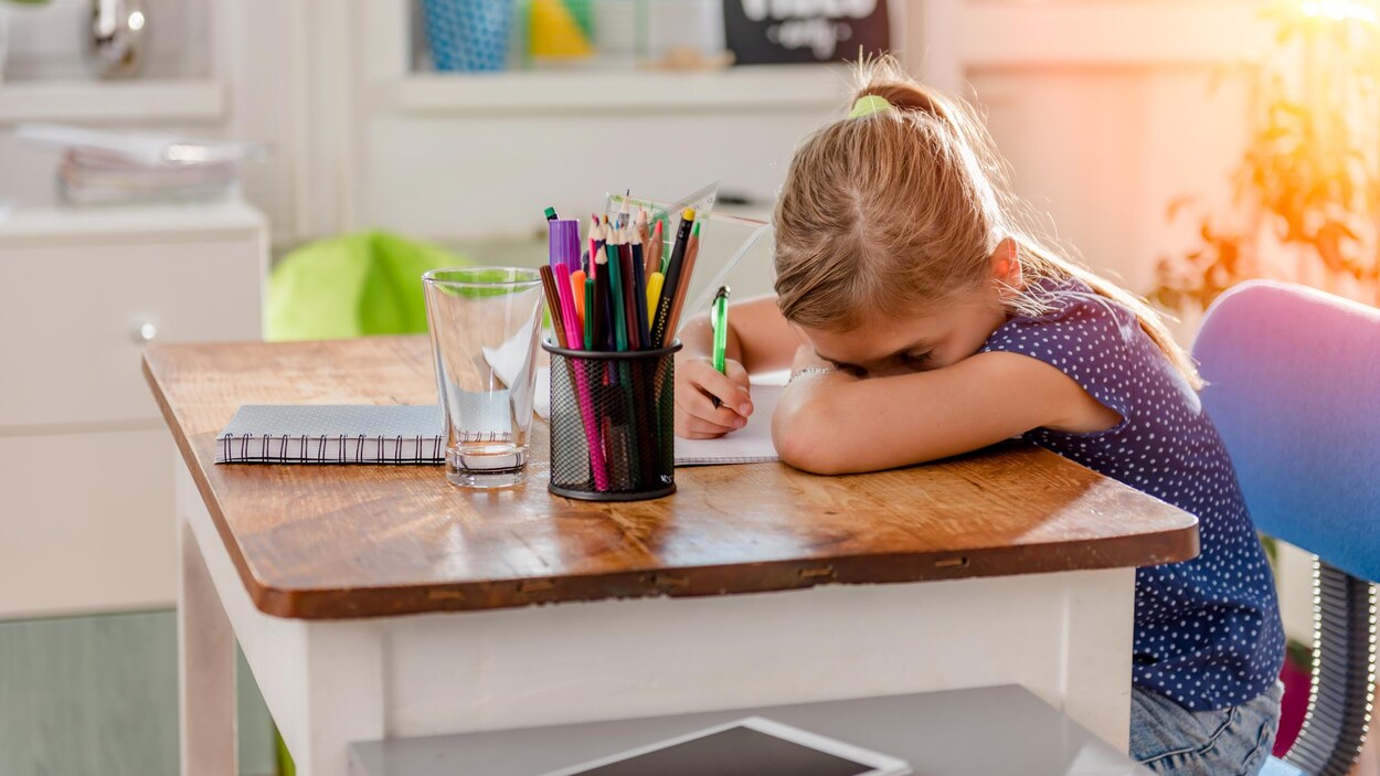 Une jeune élève semble avoir du mal à se concentrer en faisant ses devoirs.