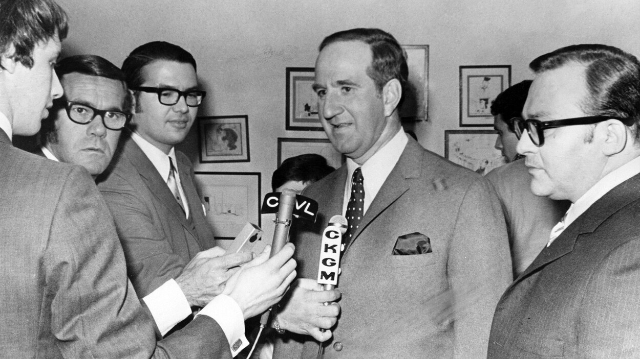 En 1970, le ministre du Travail du Québec Pierre Laporte est entouré de journalistes et de micros.