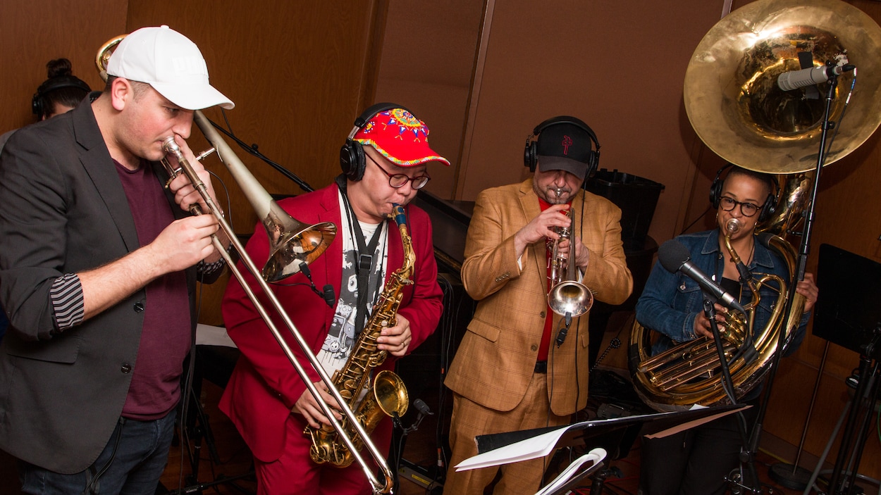On voit les quatre musiciens souffler dans leurs instruments.