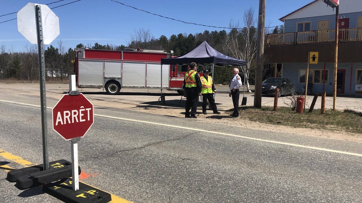 Trois pompiers sont postés sur le chemin principal. Un panneau d'arrêt est bien en évidence.
