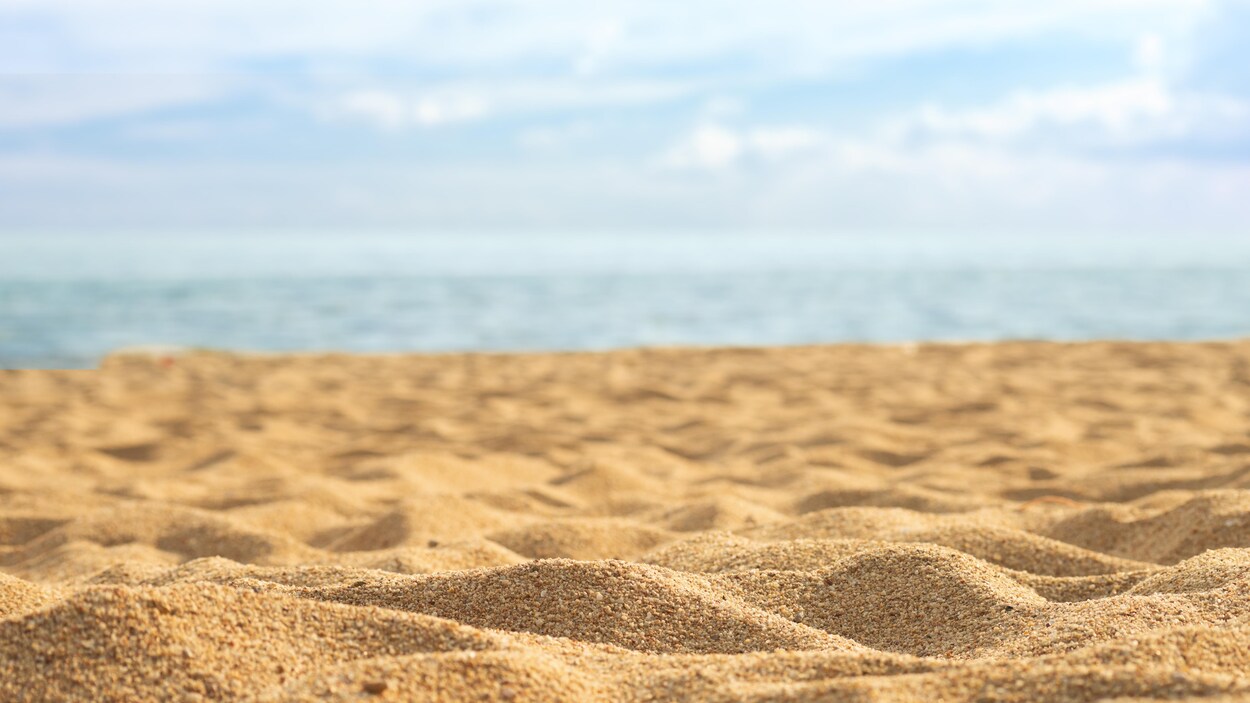 Une plage avant du sable à l'avant plan et de l'eau en arrière-plan.