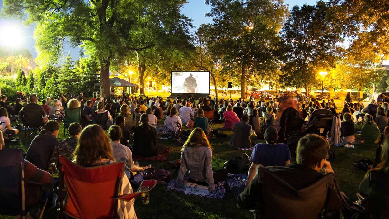 Des gens assis sur des chaises assistent à une projection de cinéma en plein air.