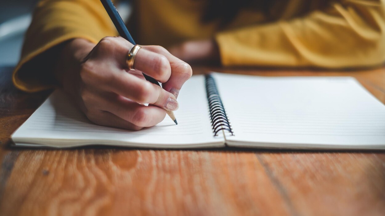 Gros plan sur la main droite d'une femme prenant des notes dans un cahier.