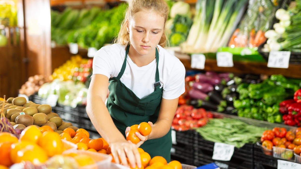 Une adolescente place des clémentines dans une fruiterie.