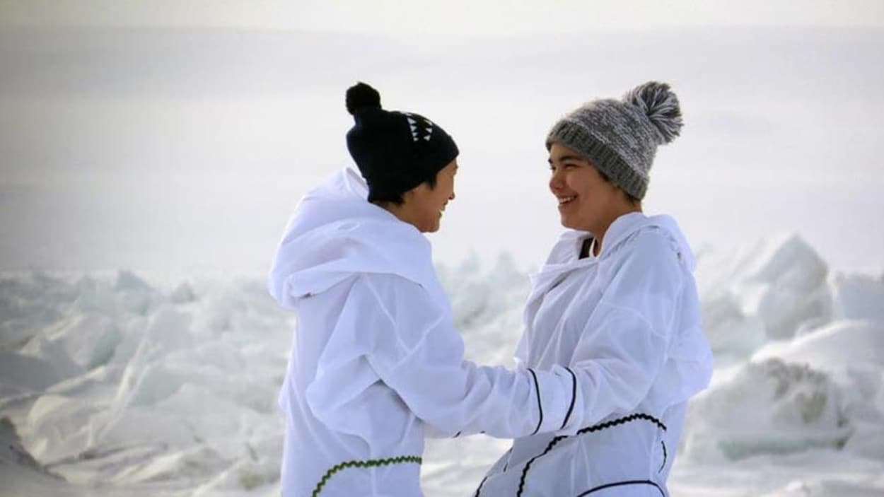 Deux jeunes chanteuses de chant de gorge éclatent de rire au terme de leur performance, devant un paysage immaculé.