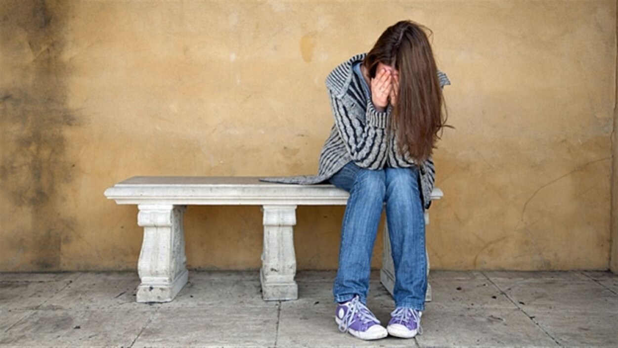 Une adolescente assise sur un banc tient sa tête entre ses mains