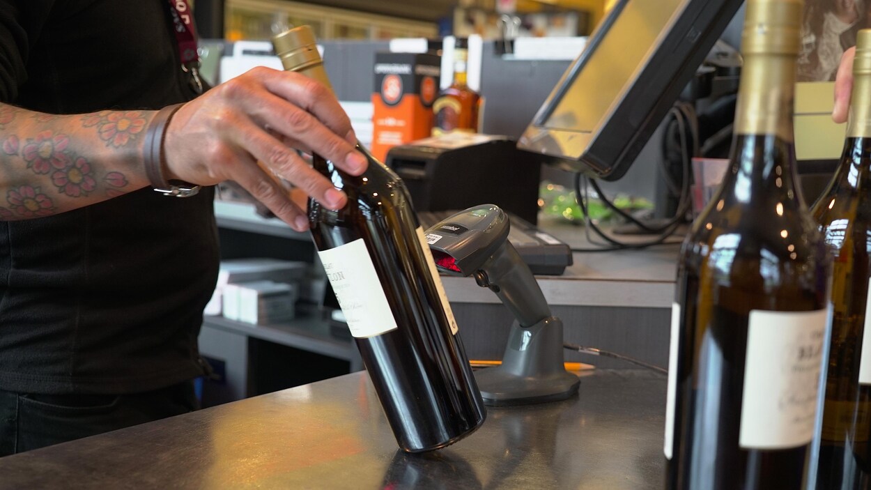 Un homme dont le bras est tatoué scanne une bouteille d'alcool à la caisse.