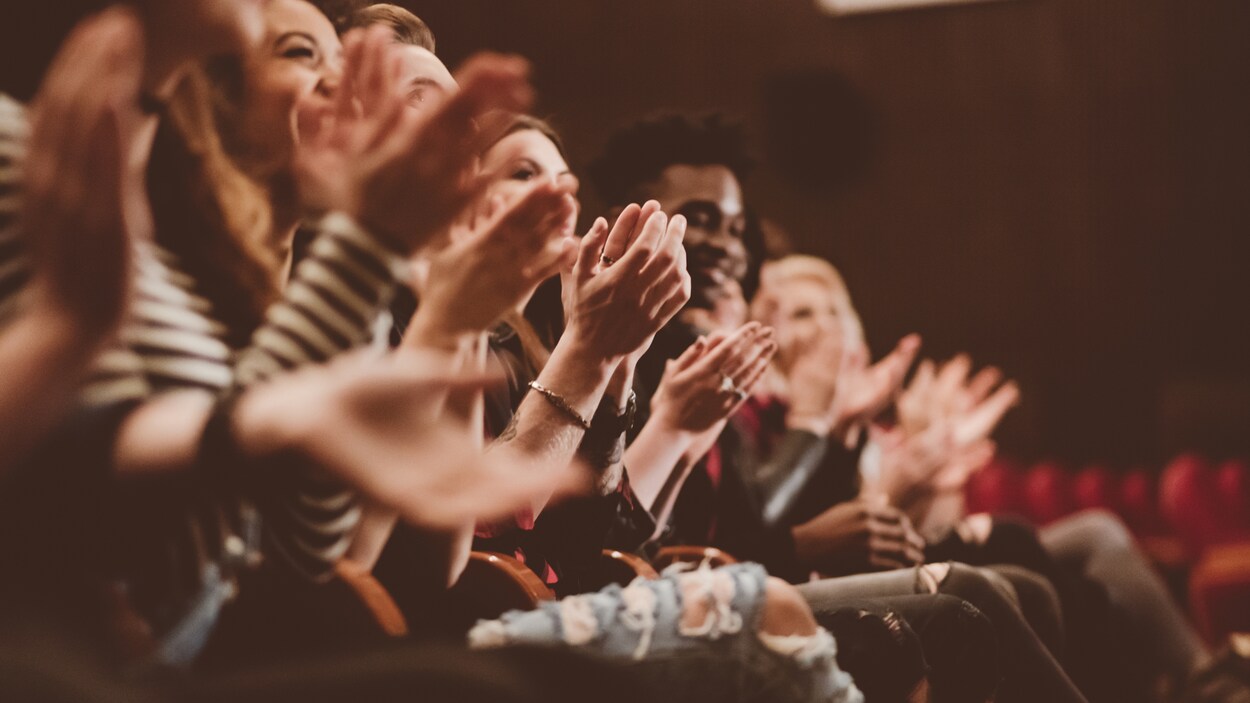 Des spectateurs applaudissent dans une salle de théâtre.