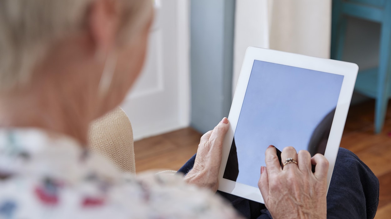 Une femme âgée manie une tablette.