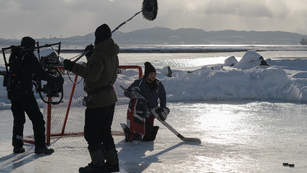 On aperçoit un caméraman, un perchiste et un comédien qui joue au hockey sur la glace.