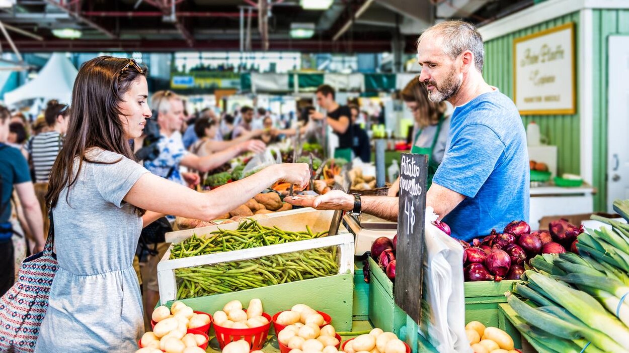 Une femme donne de la monnaie à un commerçant pour acheter des légumes.