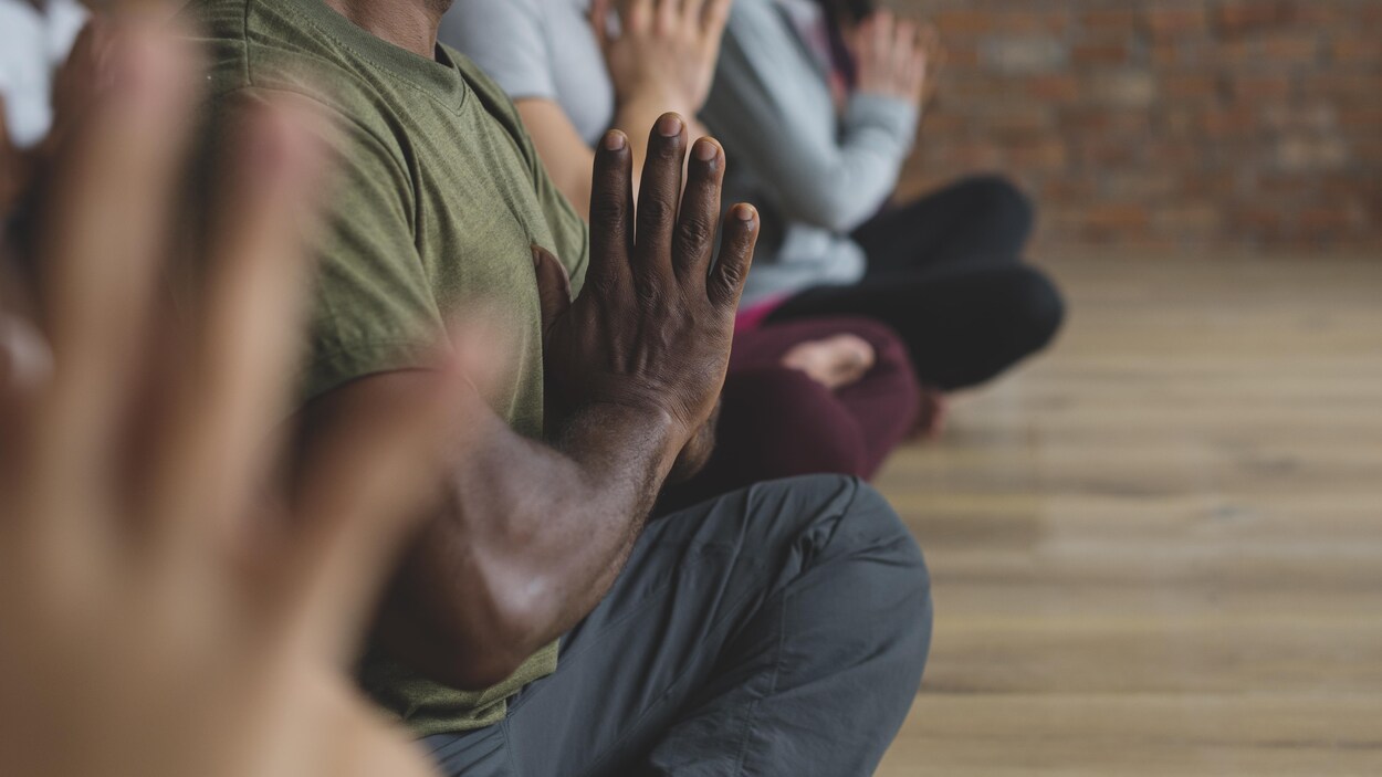 Un homme médite les jambes croisées et les mains jointes dans une classe de yoga.