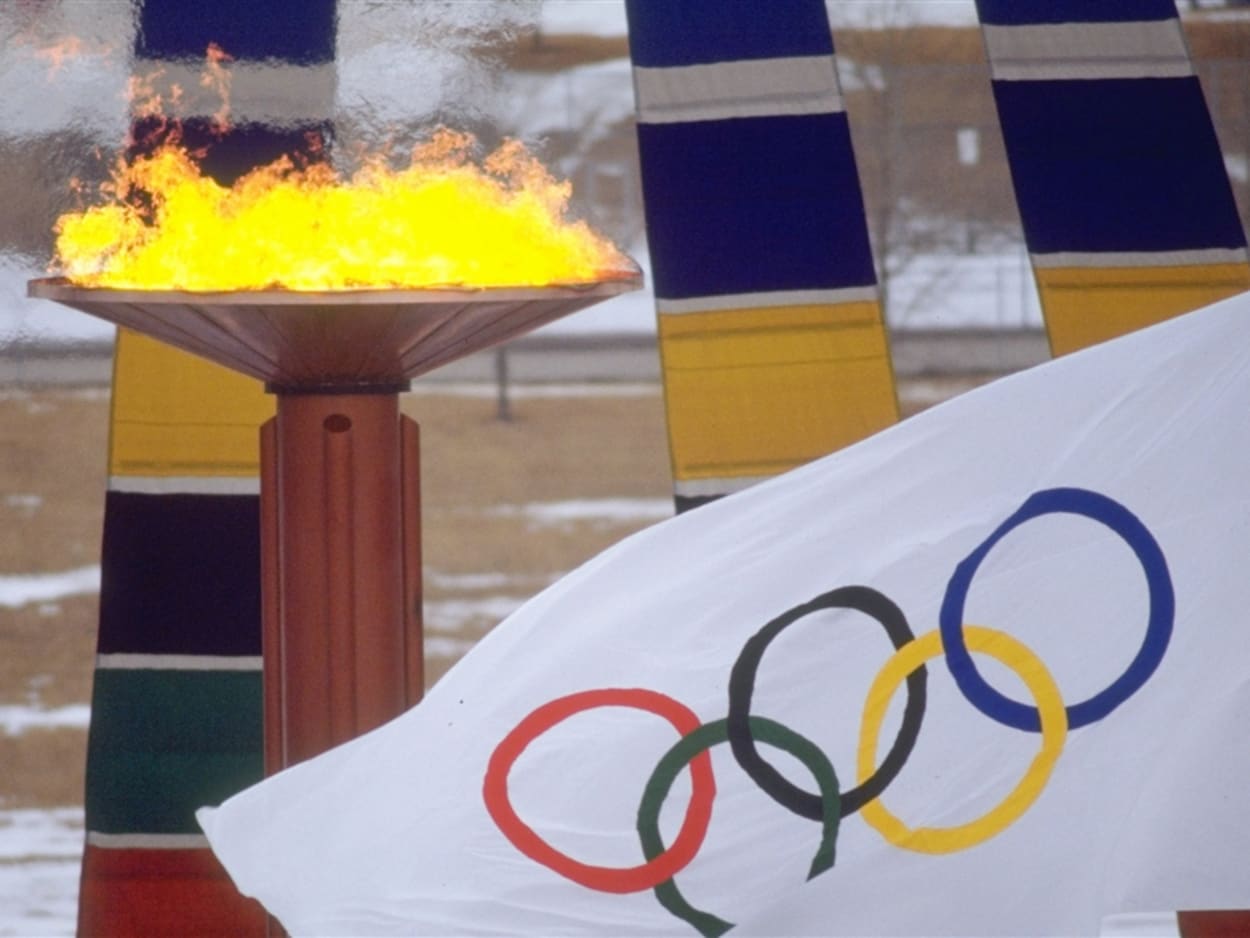 Un drapeau blanc paré des anneaux olympiques flotte devant la vasque de bronze où brûle la flamme olympique. Un drapeau blanc paré des anneaux olympiques flotte devant la vasque de bronze où brûle la flamme olympique.