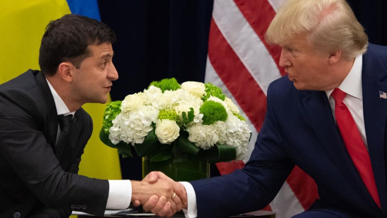 Deux hommes en complet se serrent la main devant un pot de fleurs et les drapeaux américain et ukrainien.