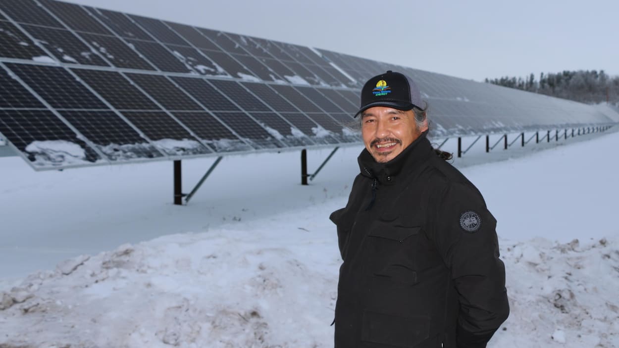Allan Adam pose devant une rangée de panneaux solaires.