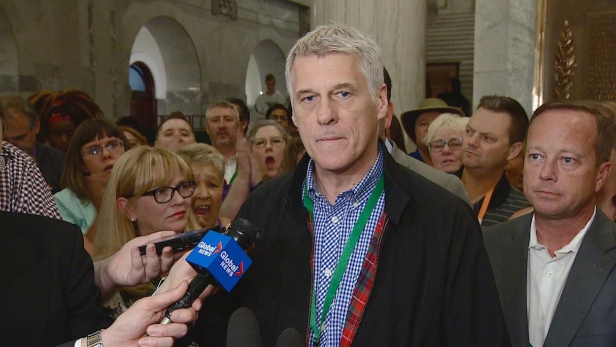 Un homme entouré de nombreuses personnes répond aux questions des journalistes au sein de l'Assemblée législative.