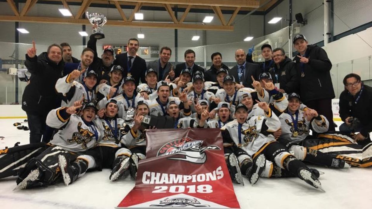 Photo d'équipe sur la glace avec la bannière de champions et le trophée.