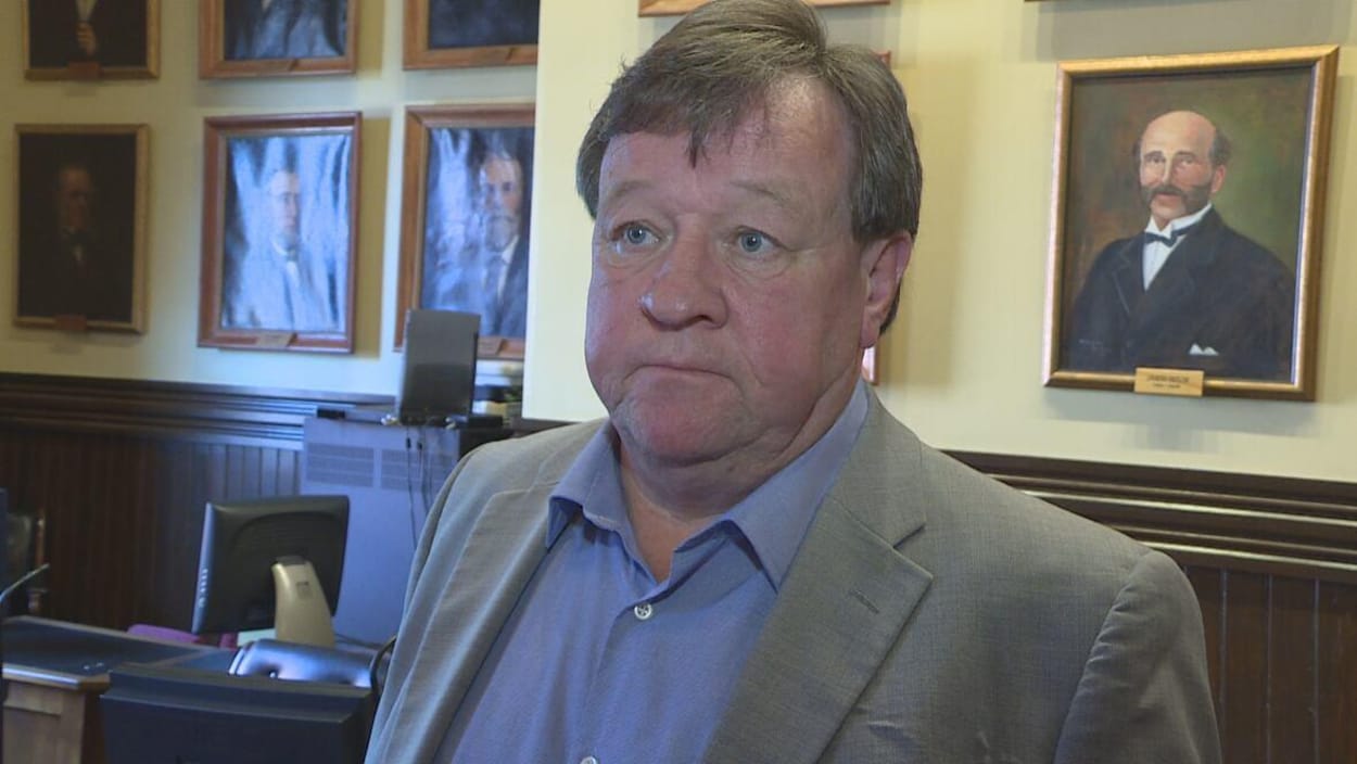 L'ancien maire de Charlottetown dans la salle du conseil municipal entouré par des portraits d'autorités.