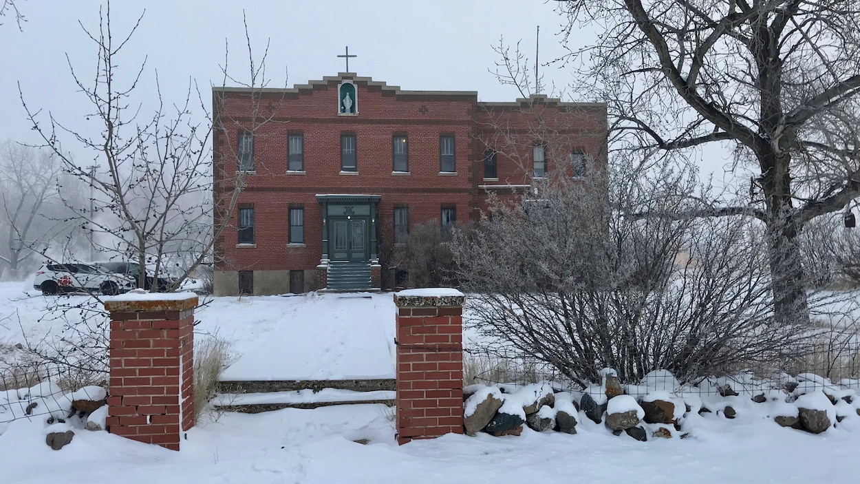 Image du couvent sous la neige. Le couvent a une croix sur le toit et une grande porte d'entrée verte.