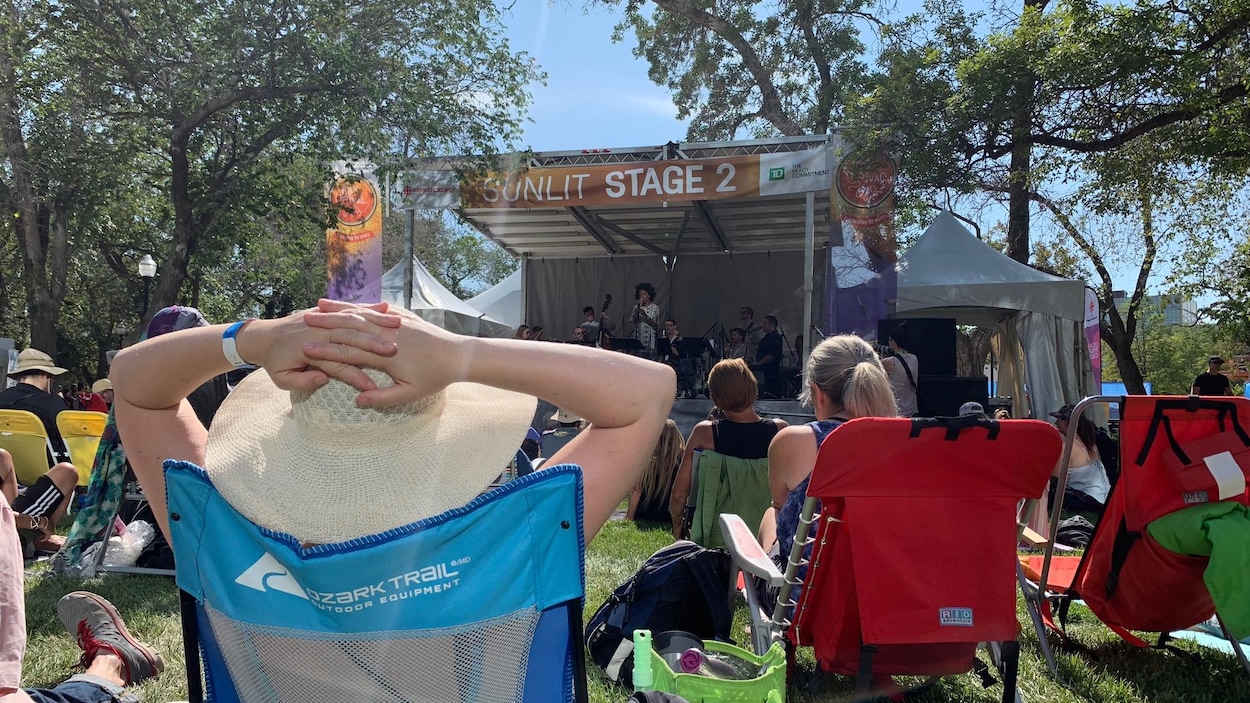 Une foule devant une scène lors d'un festival de musique à l'extérieur, en été.