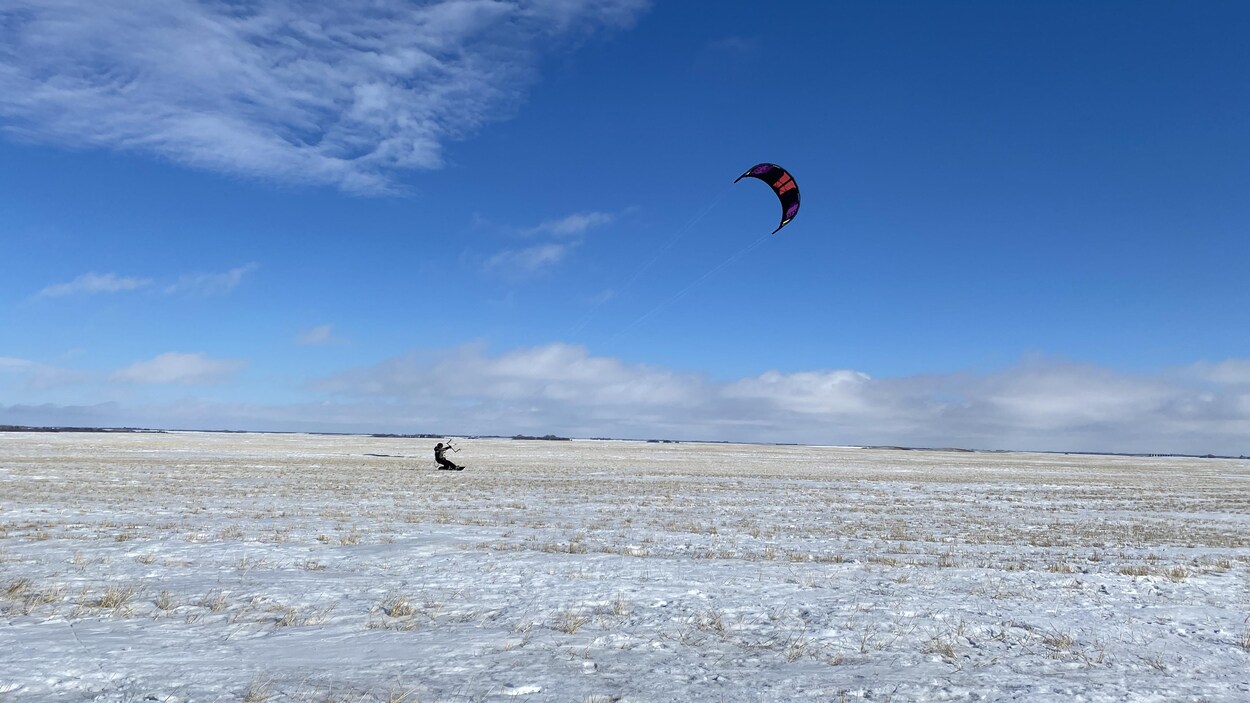 Un kitesurfer contre un ciel bleu. Il y a peu de neige dans le champ. 