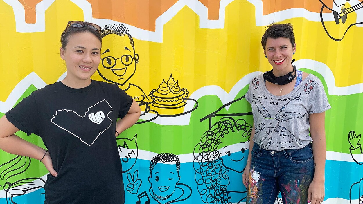 Deux femmes devant une murale colorée.