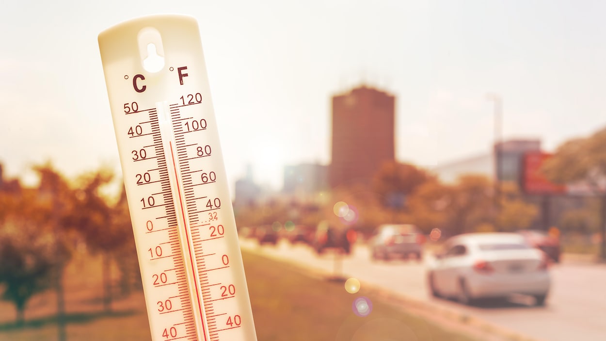 Un thermomètre devant un paysage urbain très ensoleillé.