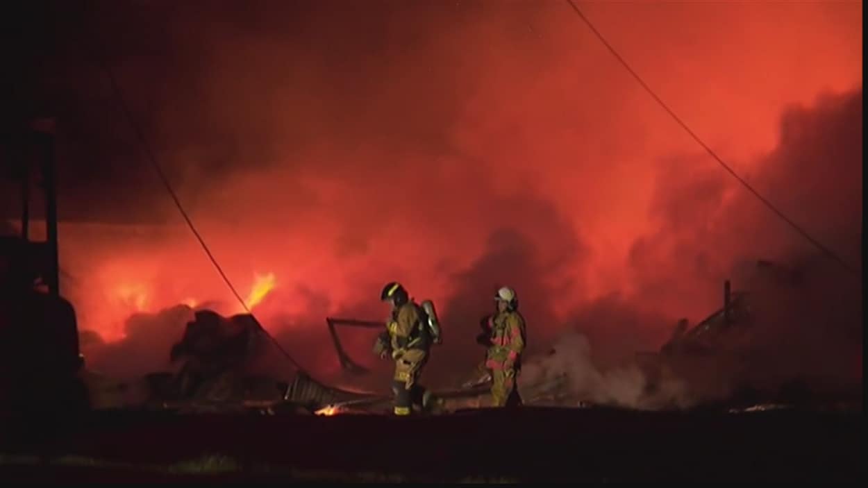 Deux pompiers marchent devant des flammes et beaucoup de fumée.