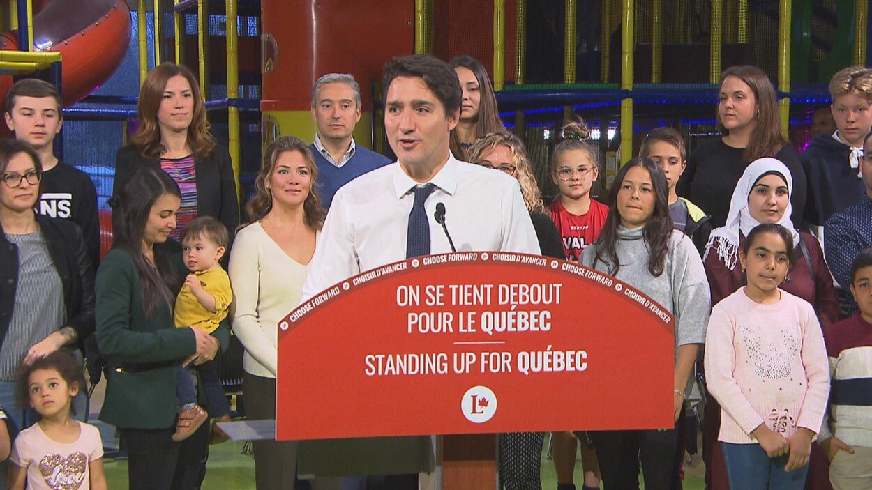 Le chef libéral Justin Trudeau au lutrin devant un groupe de femmes et d'enfants.