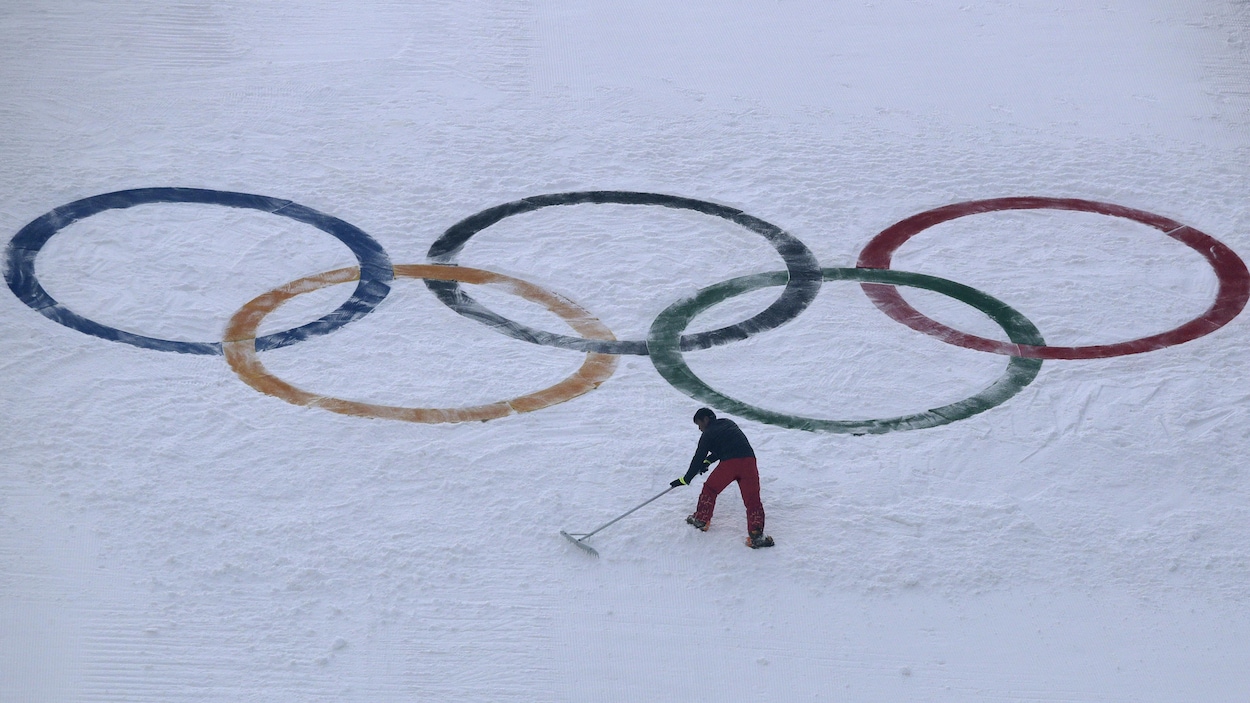 Un employé ratisse la neige devant les anneaux olympiques.