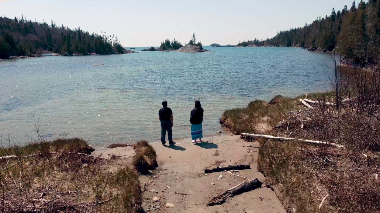 Un homme et une femme qui regarde un grand lac debout sur une plage.