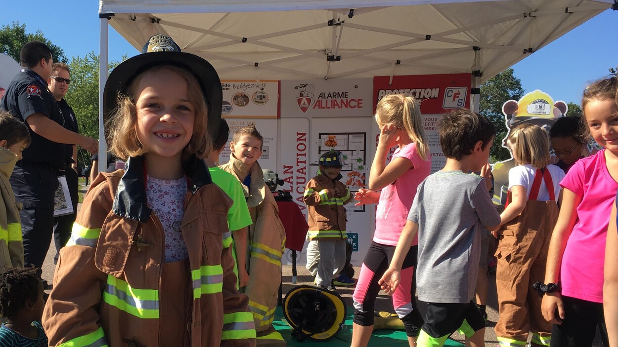 Fillette habillée d'un costume de pompiers avec d'autres enfants qui enfile des habits à l'arrière