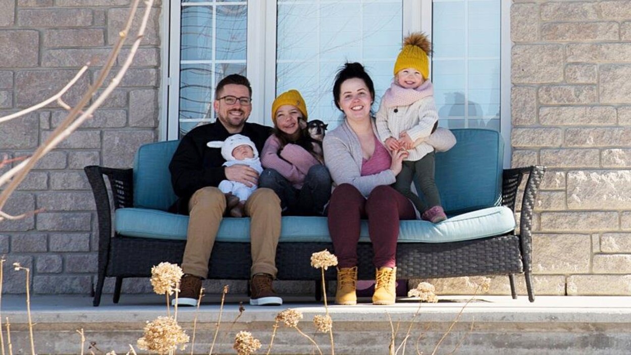 Un couple avec leurs trois enfants et un chien assis sur un fauteuil à l'extérieur.