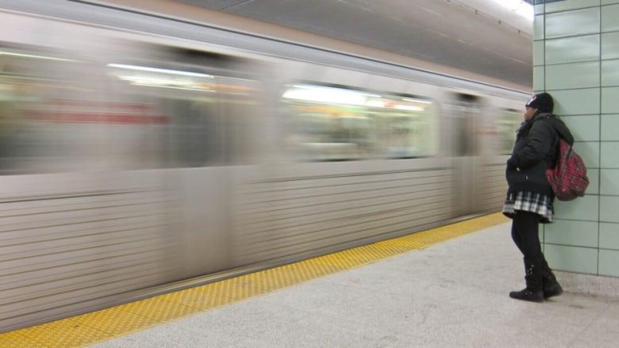 Une femme s'adosse à un mur pendant qu'un métro passe devant elle