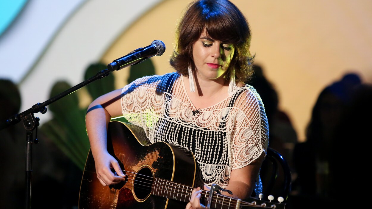 Lisa LeBlanc est assise sur un tabouret et joue de la guitare sur un plateau de télévision.