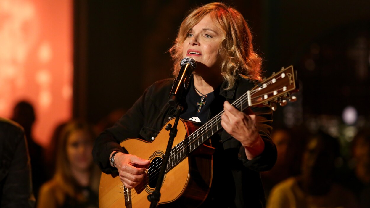 L'artiste, guitare à la main, chante.