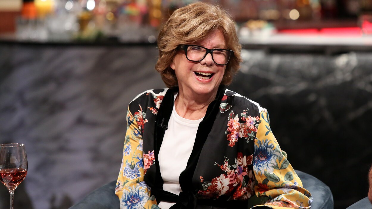 Elle porte une longue veste à fleurs, de style kimono.