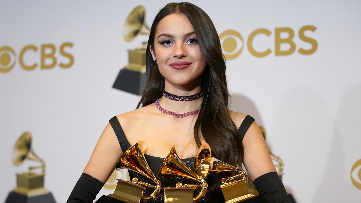 Olivia Rodrigo est debout avec trois prix Grammy dans ses mains.