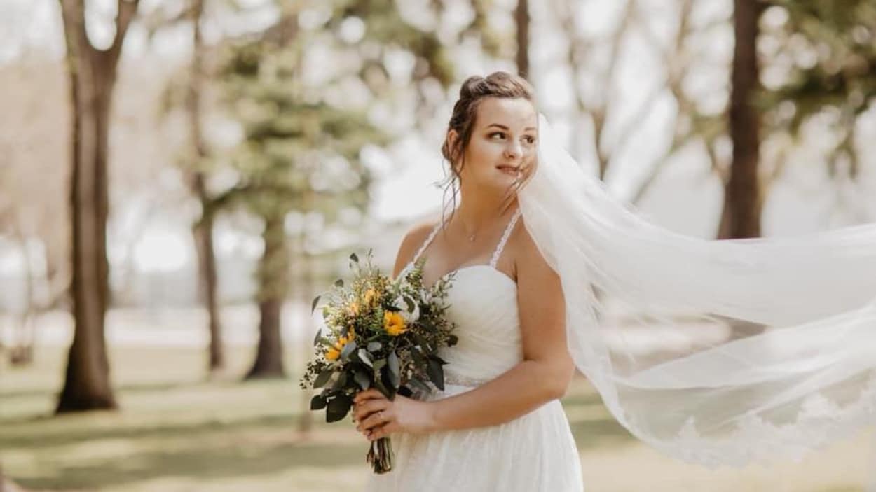 Une femme vêtue d’une robe de mariée blanche dans un parc. Elle tient dans les mains un bouquet de fleurs.
