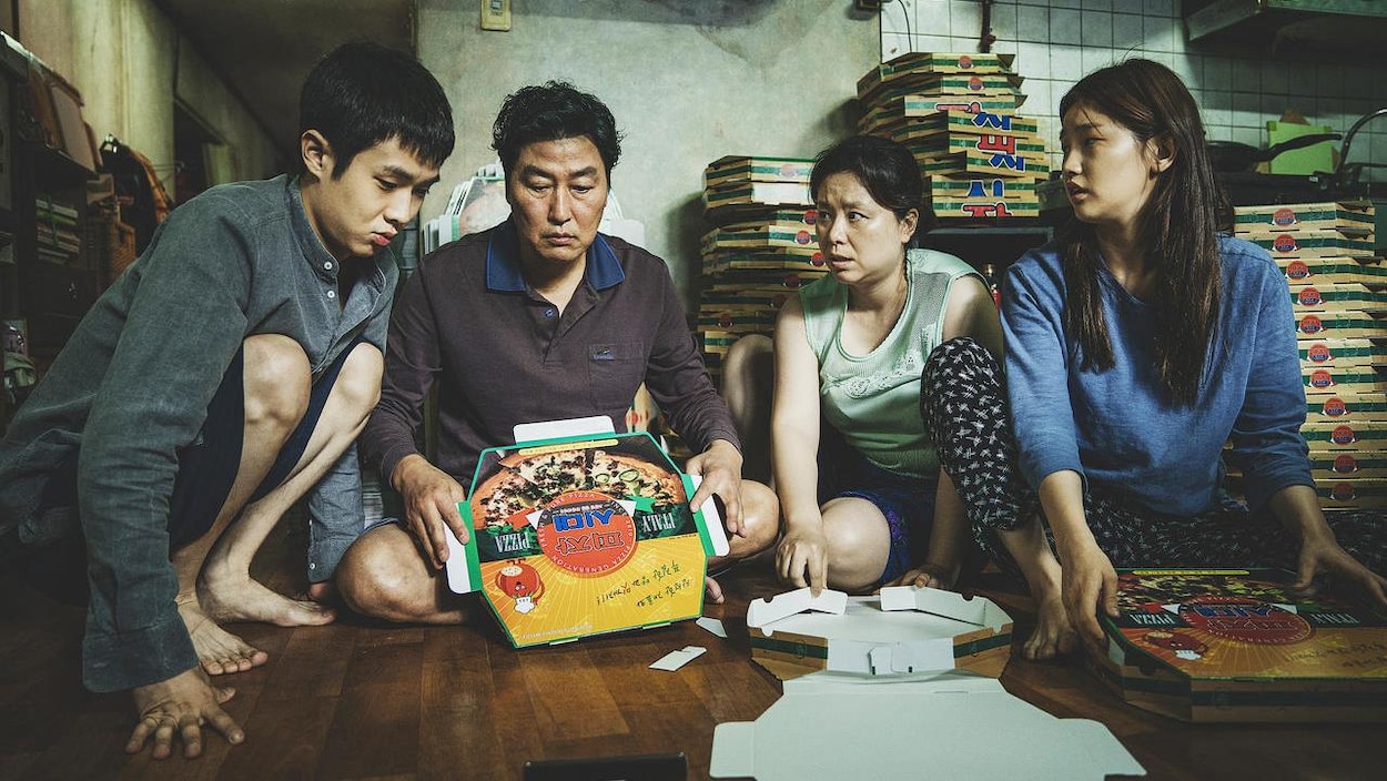 Une famille de quatre assise par terre, autour d'un carton de pizza.