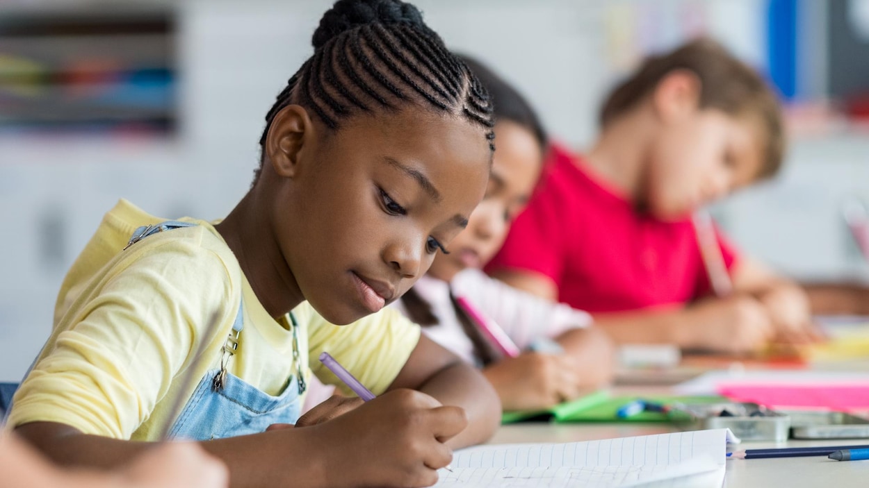 Une jeune fille est en train d'écrire dans un cahier dans une salle de classe. 