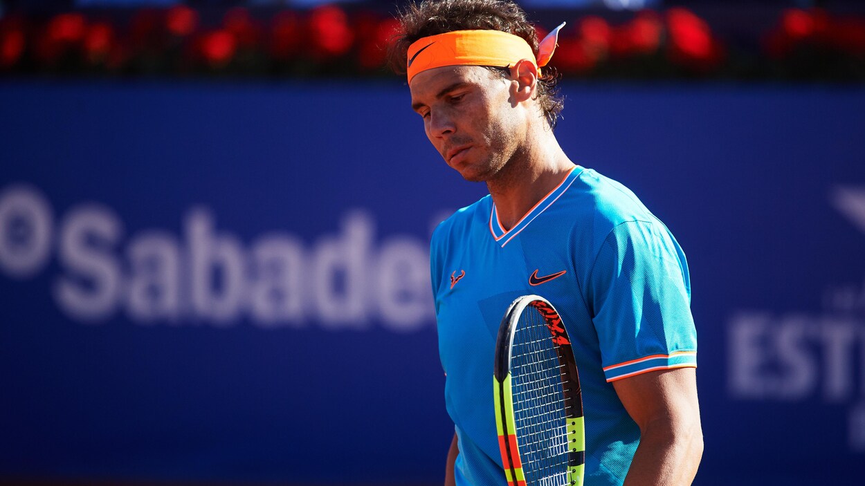 Rafael Nadal regarde vers le bas lors d'un match. En arrière-plan, il y a une bande bleue.