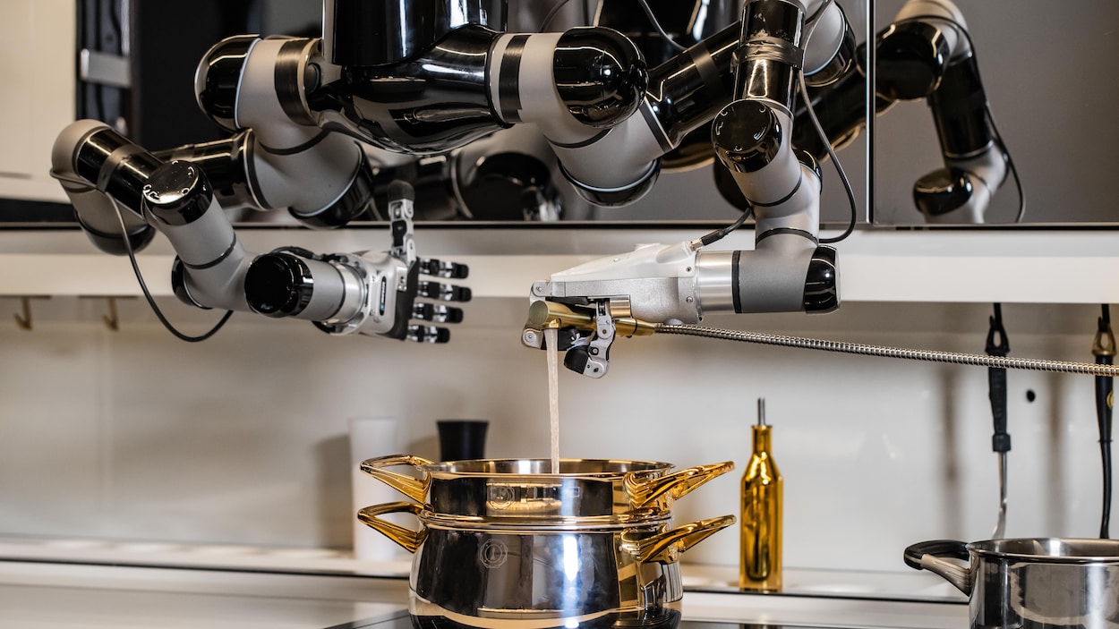 Un robot à deux bras est suspendu au-dessus d'une cuisinière. Une main robotique donne un coup de pouce et l'autre main verse de l'eau dans une marmite.