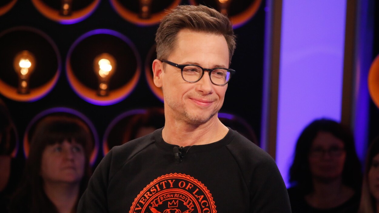 Il porte des lunettes et un chandail noir avec un logo rouge.
