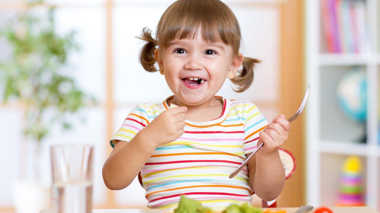 Une petite fille qui porte des couettes sourit en mangeant des légumes
