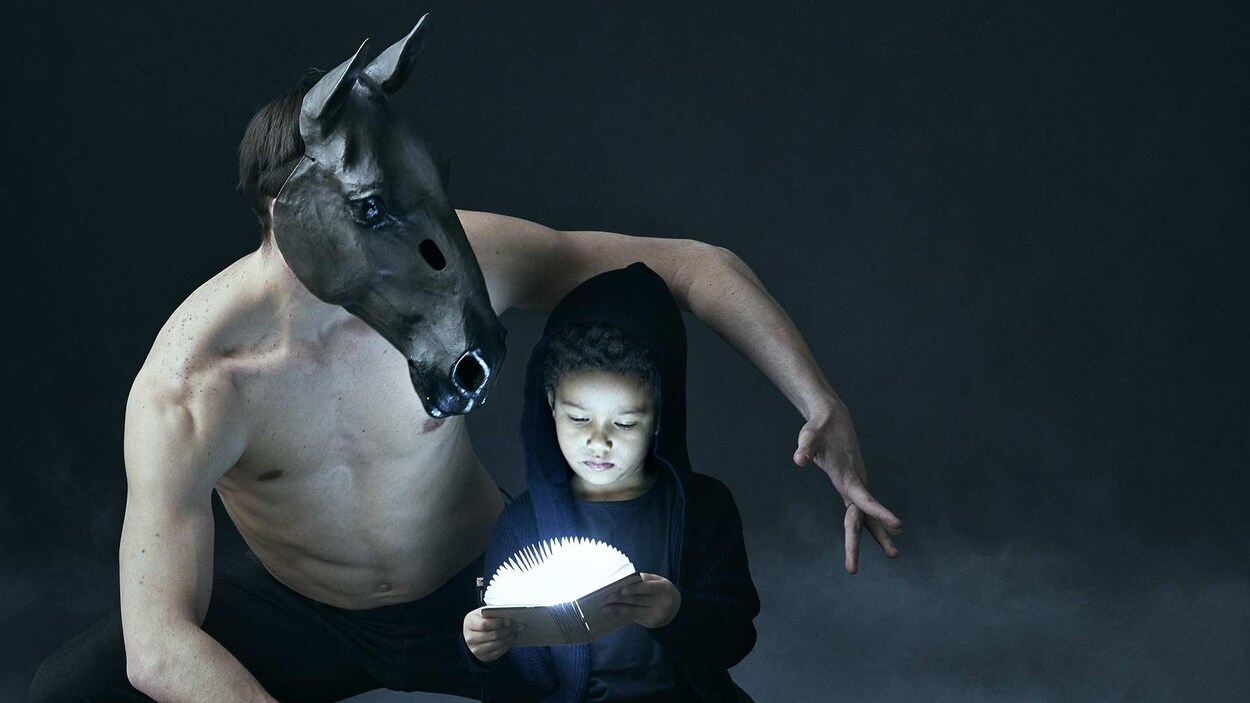 Un enfant ouvre un livre lumineux à côté d'un danseur portant un masque de cheval.