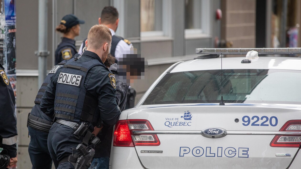 Des policiers font rentrer un homme dans une voiture du Service de police de la Ville de Québec.